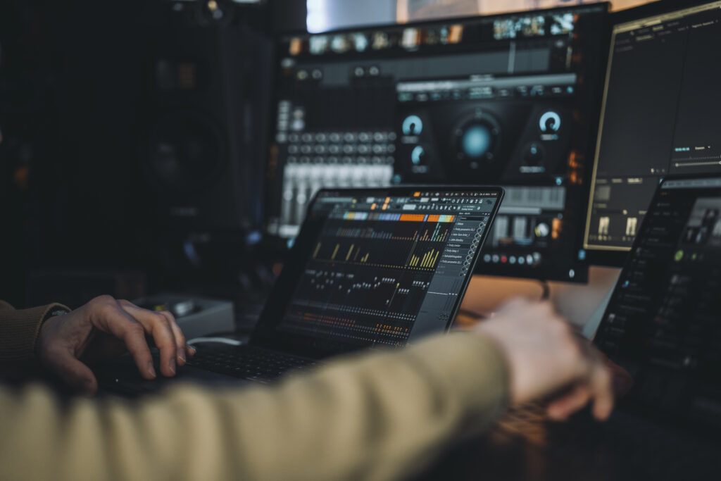 Eine Person arbeitet in einer Online Mixing Session gemeinsam am Laptop, im Hintergrund Bildschirme mit Mixing Plugins